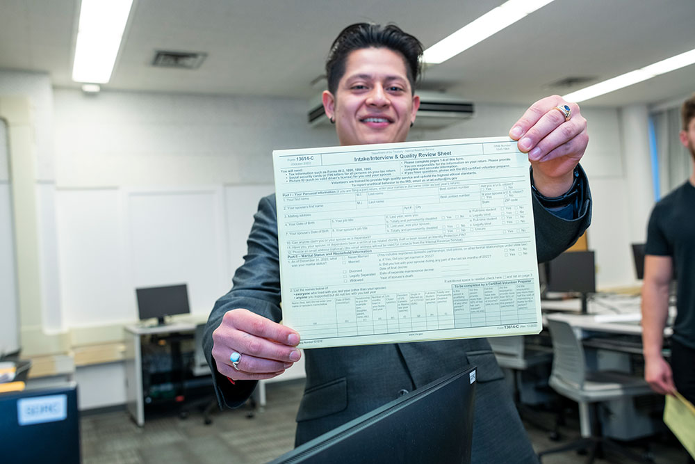 student smiling and holding up a tax form for the camera