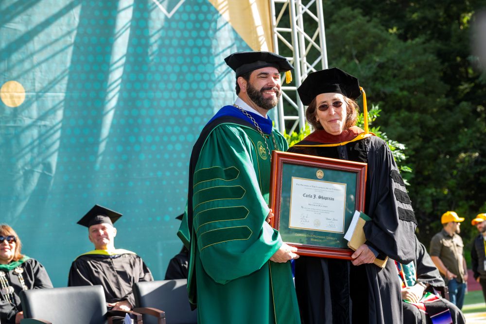A photo of President Richard A. Carvajal presenting the Honorary Doctorate of Fine Arts to Carla Shapreau. 