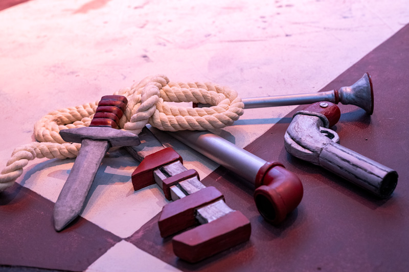 An assortment of prop weapons, such as blades and firearms, lying haphazardly on the ground, highlighting their different styles on the set of Clue