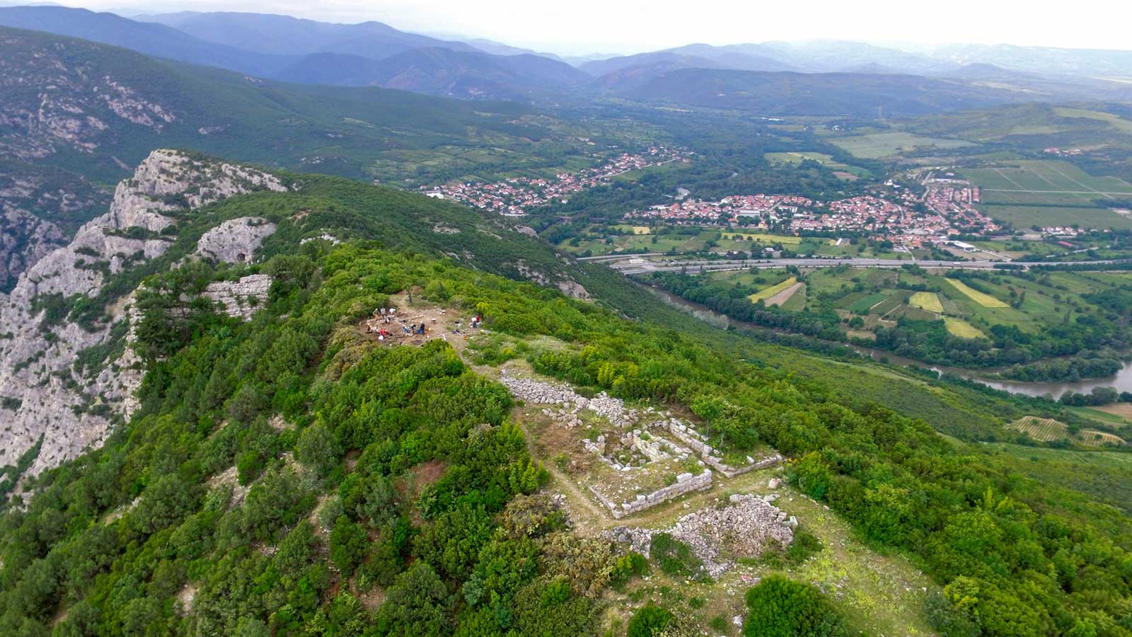 Aerial view of a village nestled in the mountains, showcasing its scenic landscape and surrounding greenery.