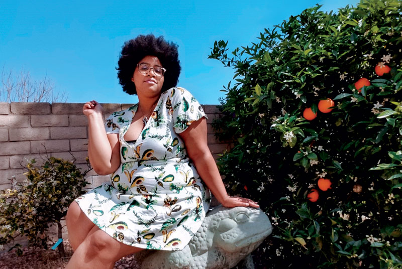 Sabina sitting next to an orange tree in front of a brick wall sitting on a frog sculpture.