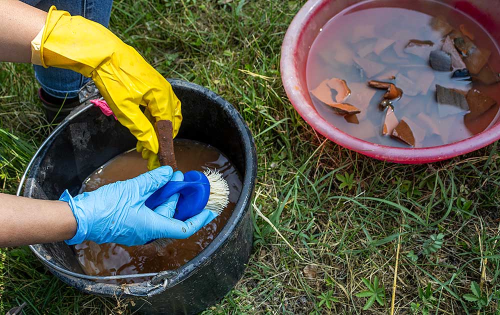 A person wearing rubber gloves cleans artifacts in a bucket filled with water