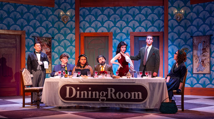 A lively dinner party scene with several people seated around a table, engaged in conversation and enjoying their meal on the set of Clue