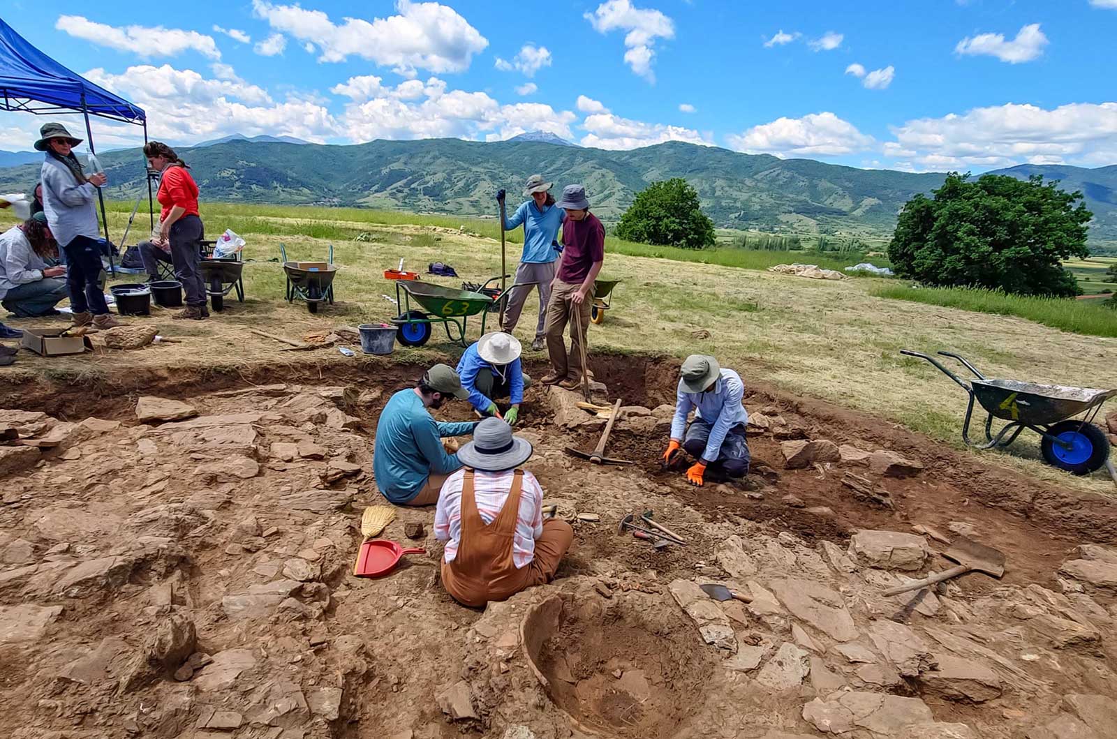People excavating at a mountain dig site, surrounded by rocky terrain and tools for archaeological work
