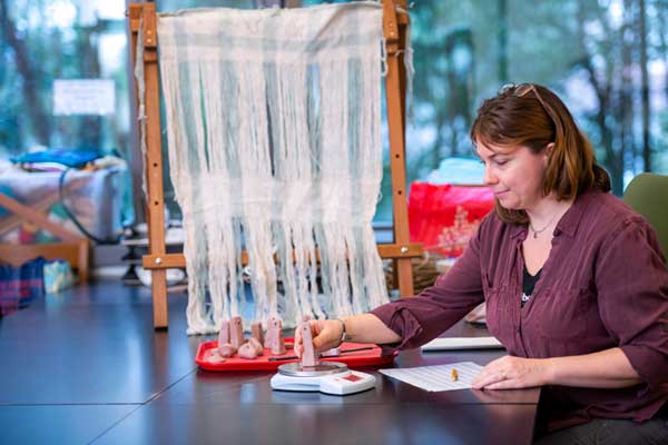 Jessica Morris Bedell works with replica loom weights in the campus Experimental Archaeology Lab, where they are tested on a warp-weighted loom visible in the background. These looms were a common weaving tool across Europe, dating back to the Neolithic period. Photo by Kellie Jo Brown. 