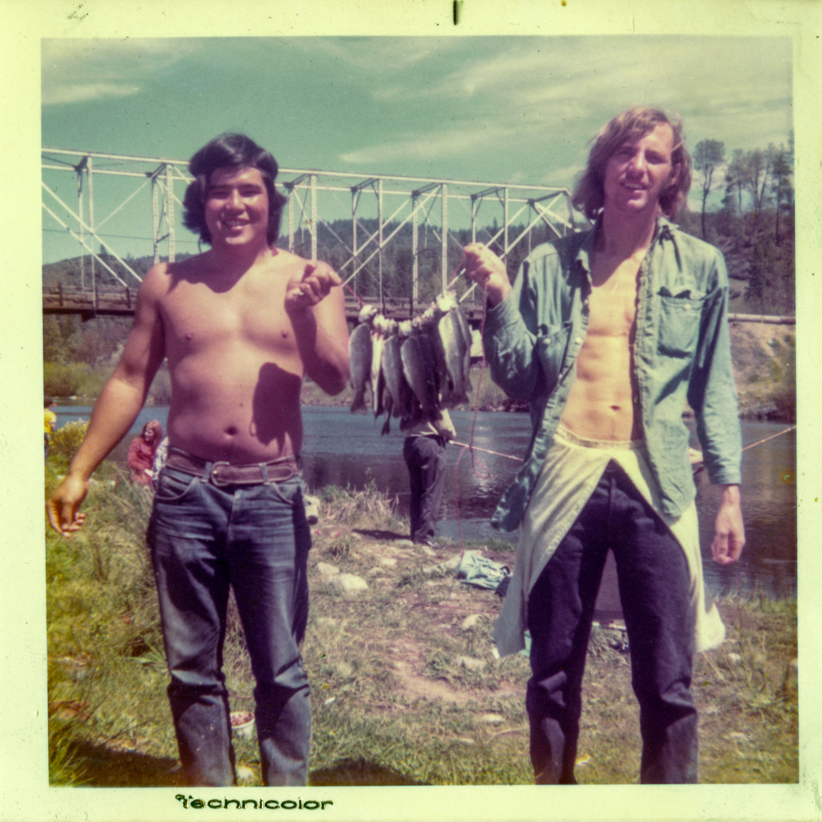 Two men proudly holding large fish, smiling at the camera, with a natural outdoor setting in the background