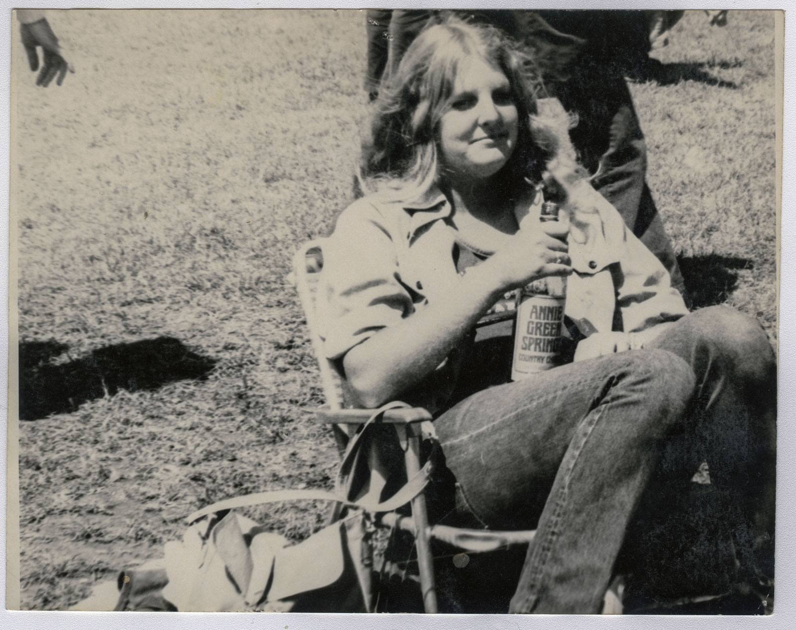 A woman sitting on a chair, casually holding a bottle of beer in her right hand