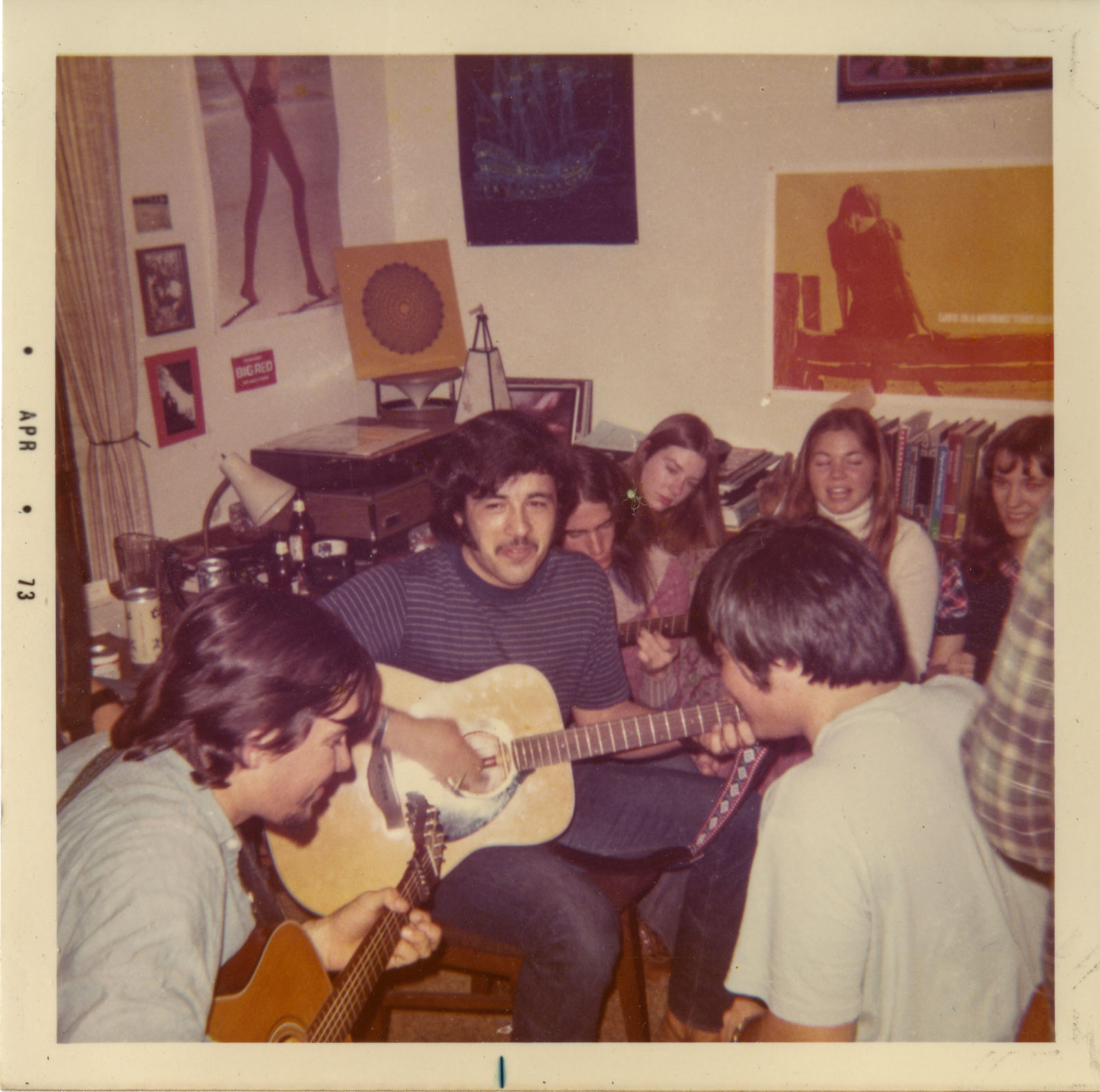 A group of people gathered in a small room, playing guitar and enjoying a collaborative music session