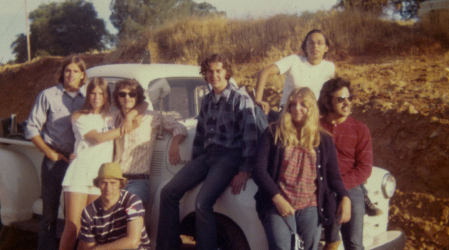 A vintage style image of a group of people smiling and posing in front of a parked truck on a sunny day
