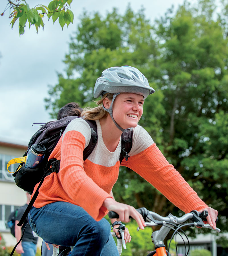female student on a bike wearing a helmet & backpack