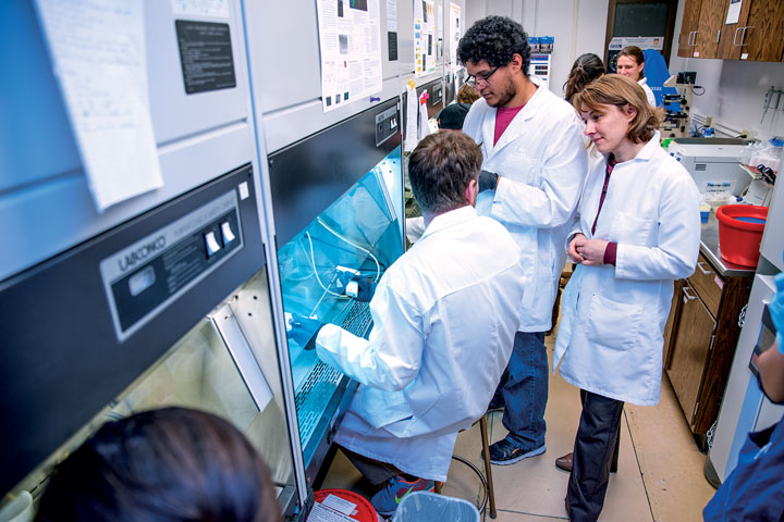 students in white coats in the lab with a professor