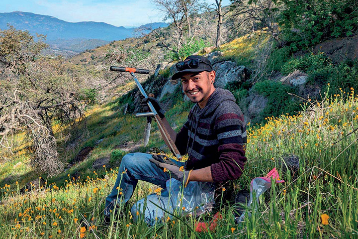 student holding a long peice of equipment on a hillside, smiling for the camera