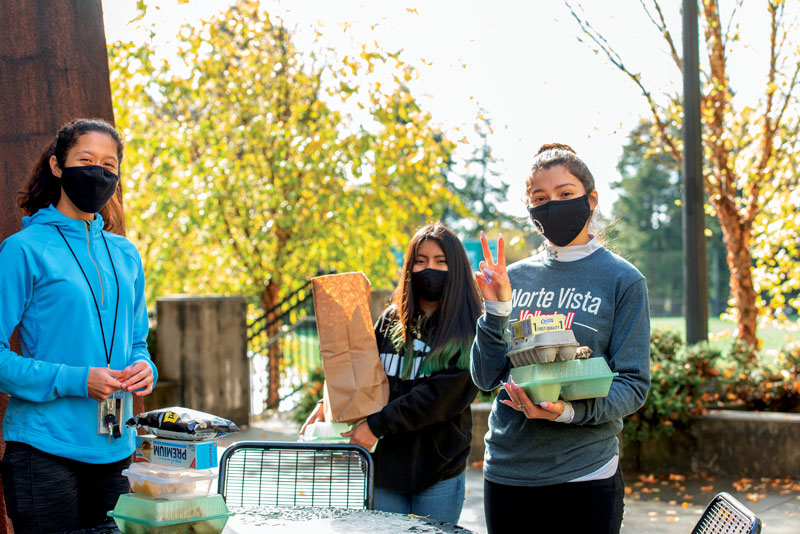three students wearing masks serving meals on campus during the pandemic