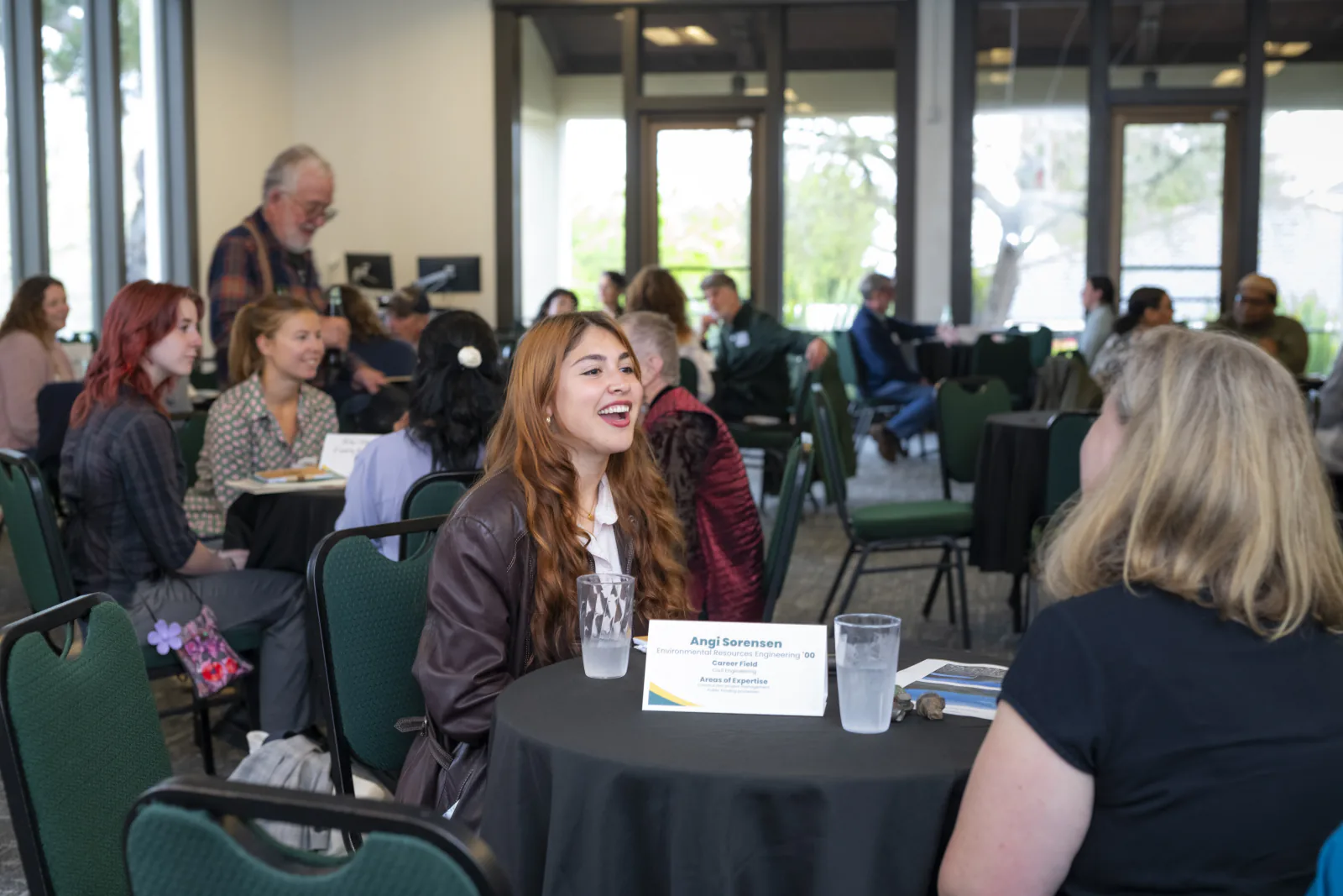 A student smiles while speaking with an alum as other Alumni Connections conversations happen around the room.