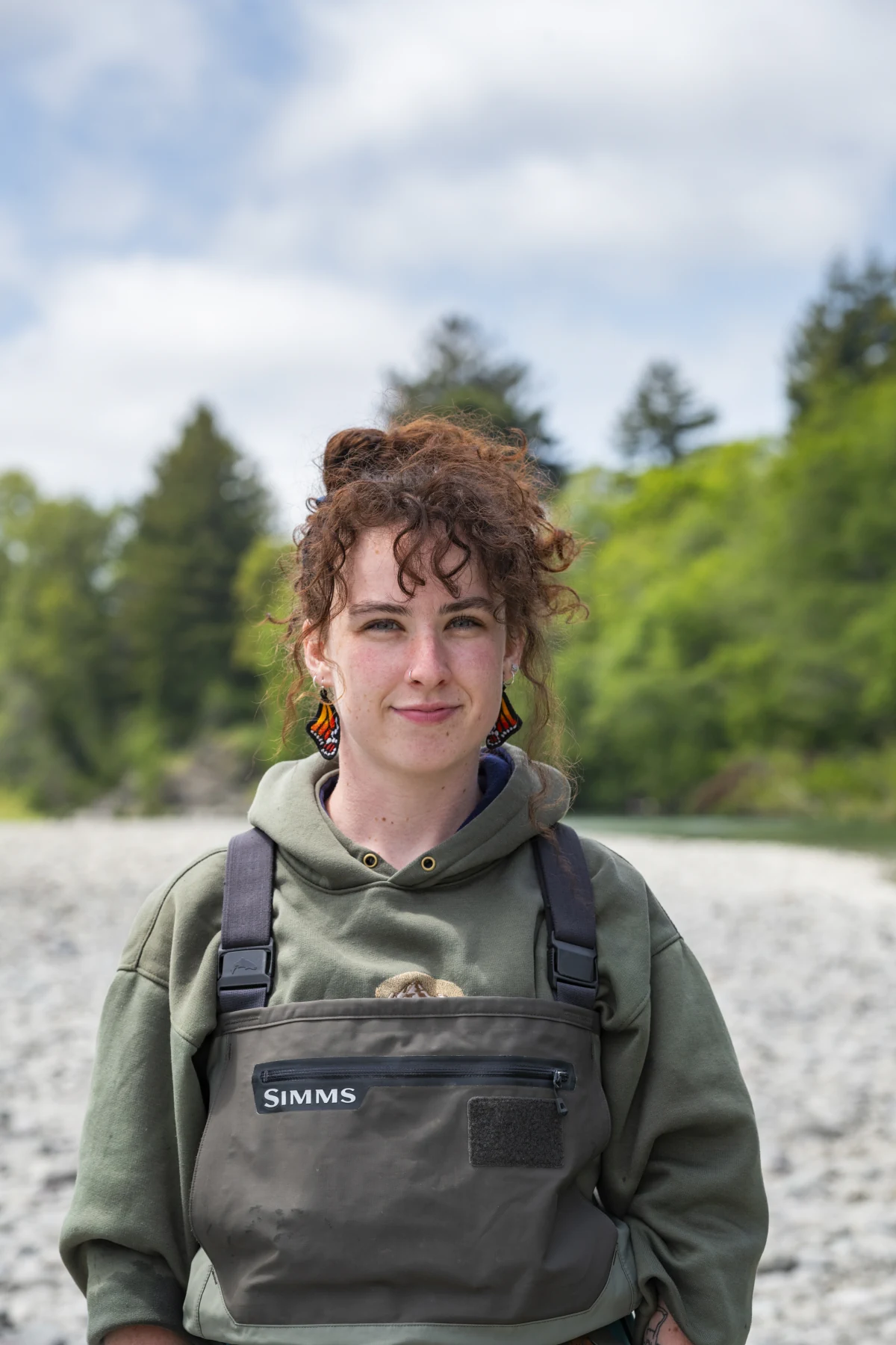 Daphne Cheney sits beside a river with a fly rod and tackle box.