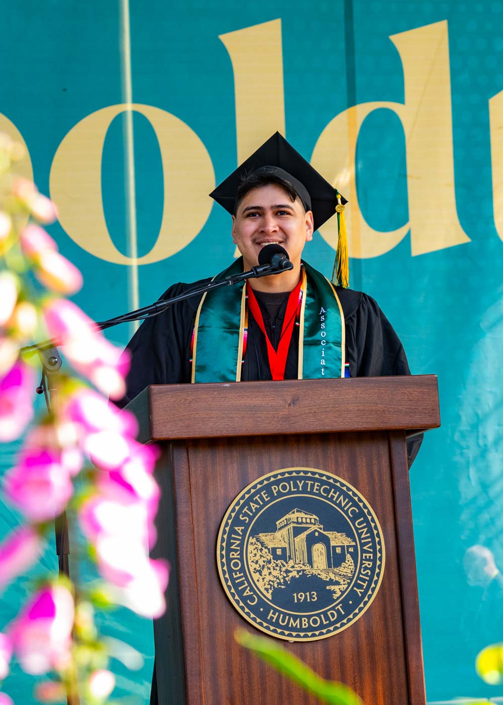 Eduardo Cruz wearing a cap and gown, sanding at a podium giving commencement speech.