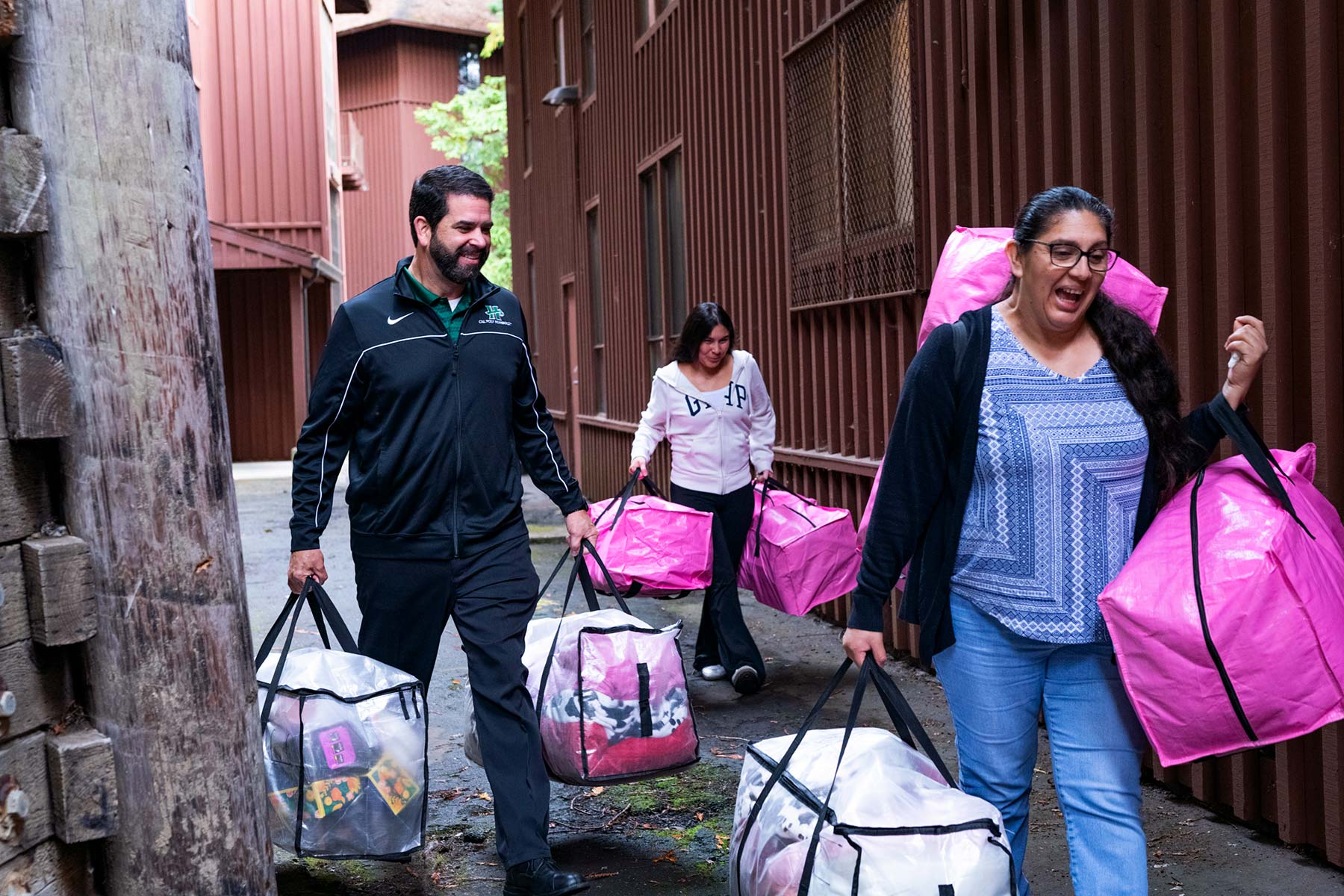 Richard Carvajal and two people carry bags through a residence hall walkway.