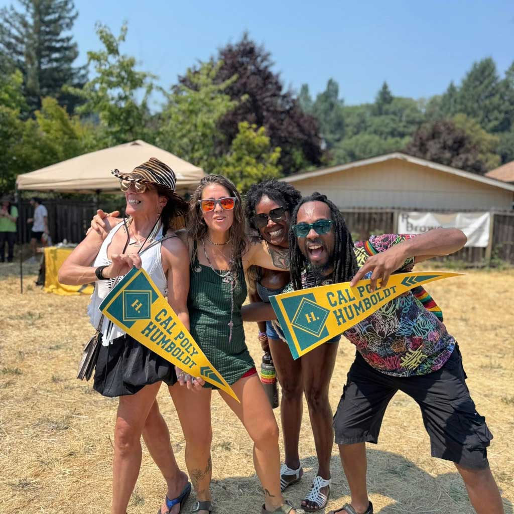 Alumni holding Cal Poly Humboldt flags with their arms around eacehother at a festival in Willow Creek for Bigfoot Daze