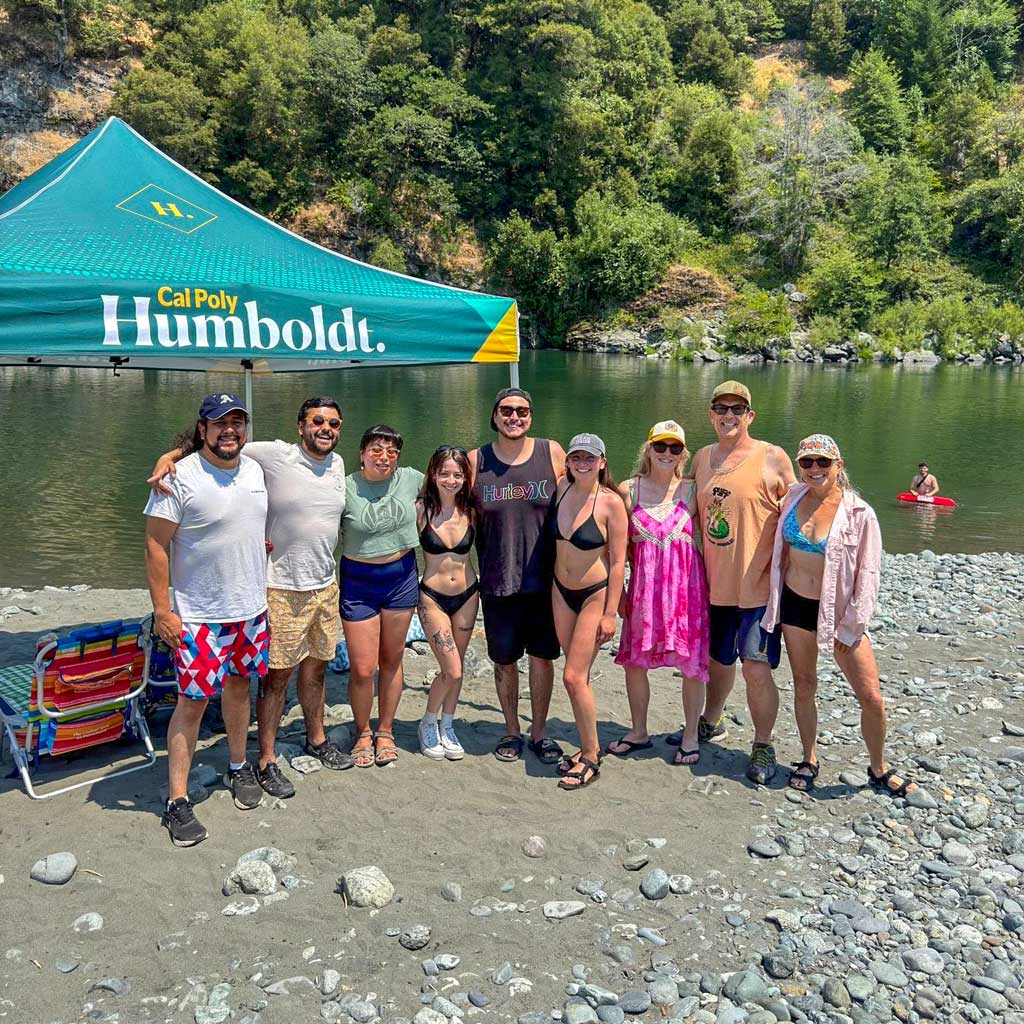 A group of people standing in a row with arms around each other in front of the river at Camp Kimtu on the Trinity River