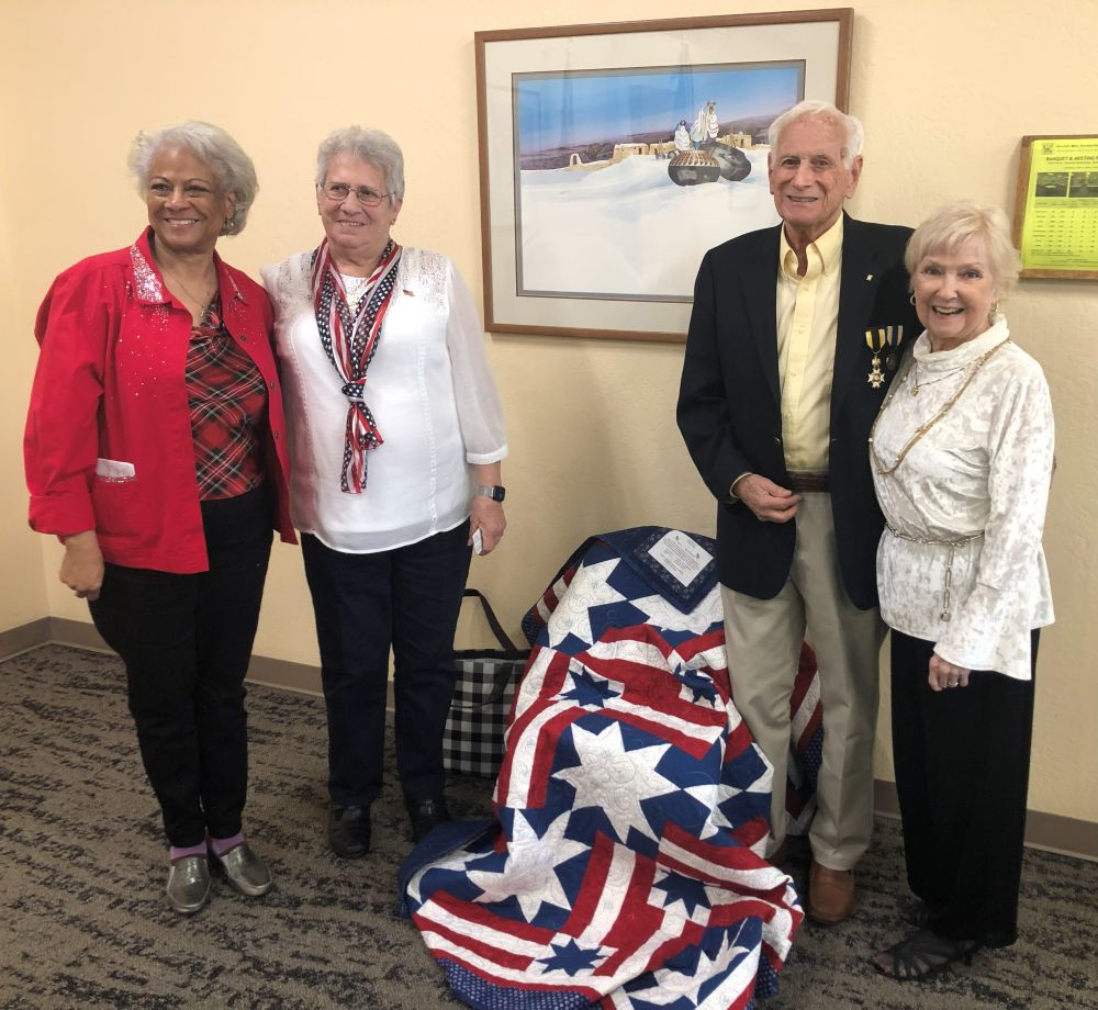 A photo of Lenore Aulenbach and Roxie Hunter presenting a quilt to Bob and Margaret Archibald. 