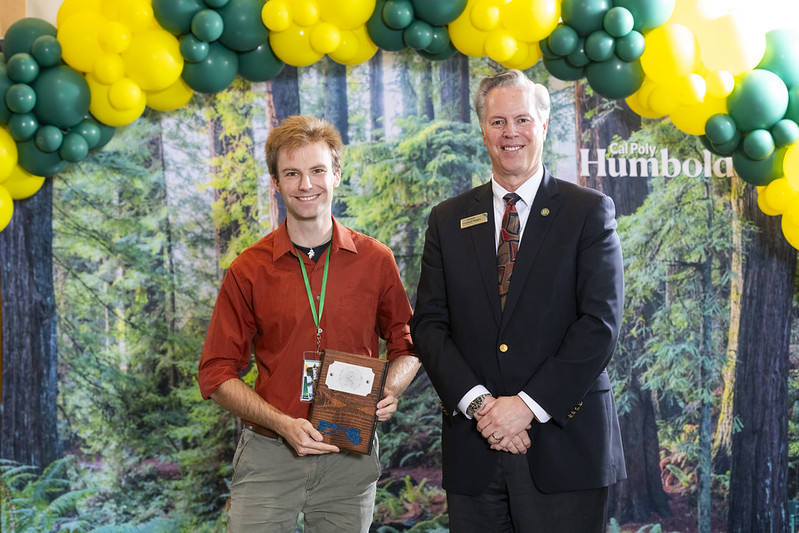 A photo of David Schmitz holding his 2nd place trophy standing next to Cal Poly Humboldt Interim President Michael Spagna.