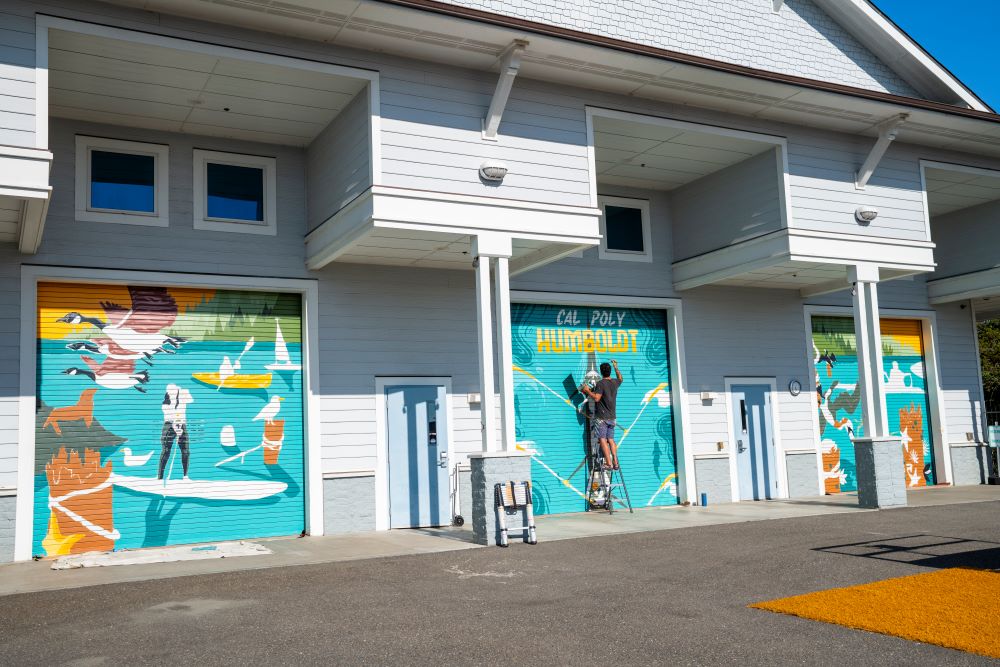 A photo of artist Tony Diaz's mural at the Humboldt Bay Aquatic Center features vibrant paintings of activities and animals found in the Humboldt Bay area.