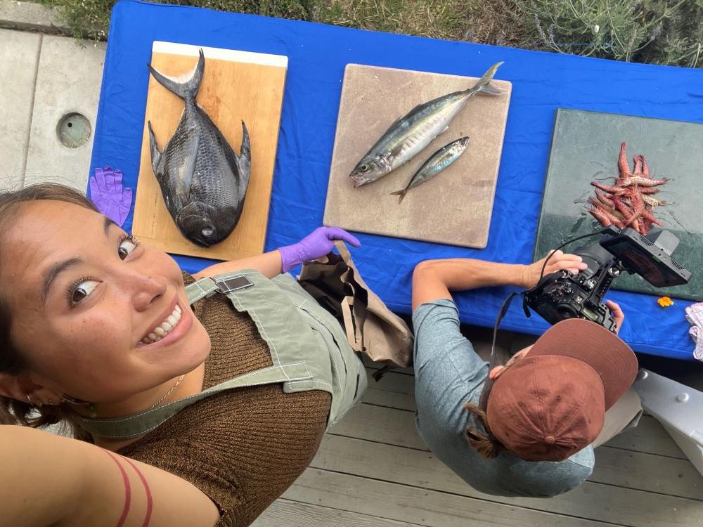A photo of Eva Sideris looking up at a camera with fish on a table below. 