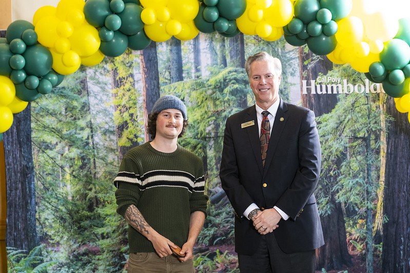 A photo of Garrett Kitchen holding his honorable mention award standing next to Cal Poly Humboldt Interim President Michael Spagna