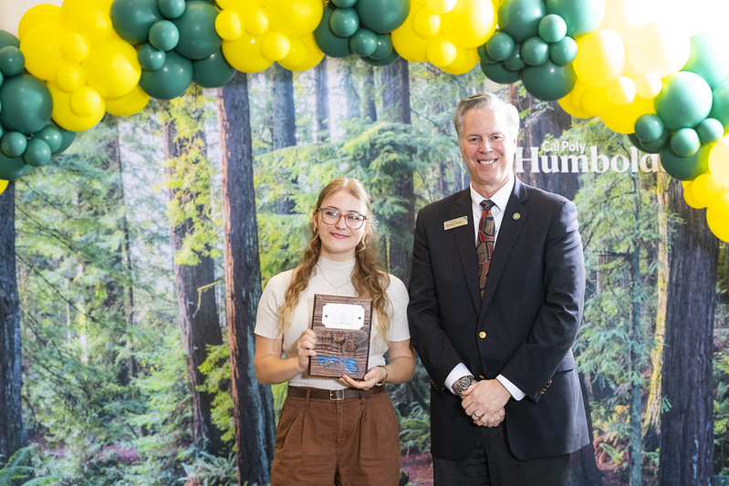 A photo of Harmony Switzer-Tryon holding her 2nd place trophy standing next to Cal Poly Humboldt Interim President Michael Spagna