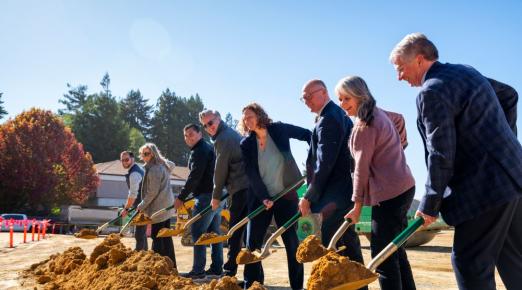 From left to right a photo of Jeff Good, Danielle Martin Spicer, Mike Fisher, Michael E. Spagna, Jenn Capps, Eric Riggs, Eileen Cashman, and Dale Oliver shoveling dirt on the construction site of the new Engineering & Technology Building, set to open Fall 2026.  