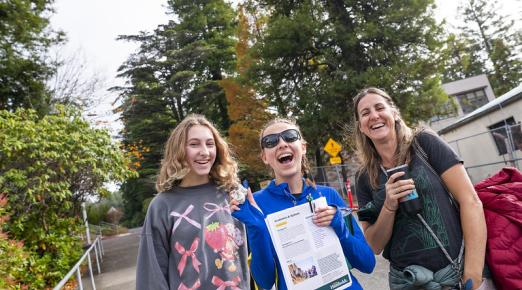 A photo of three women; one is a prospective student holding a rock in one hand and an informational booklet about the majors she can study at Cal Poly Humboldt during a University Preview event.