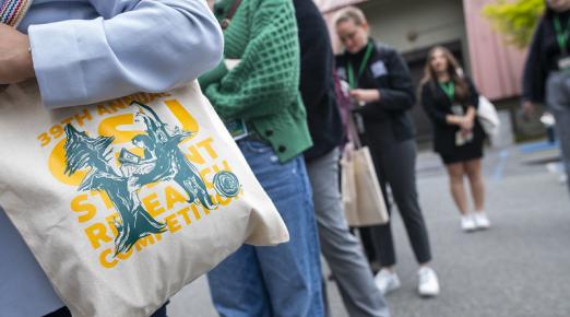 A photo of a person standing in line with a tote bag that displays the 39th annual CSU Research Competition logo.
