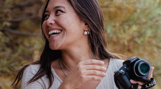 A photo of Eva Sideris smiling and looking right while holding a camera.