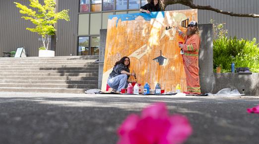 Two students and Professor James Woglom painting a large mural outside on the Art quad.