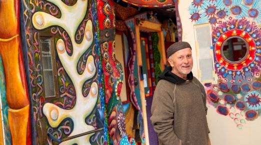 A photo of artist David White posing in front of the art hallway he created.
