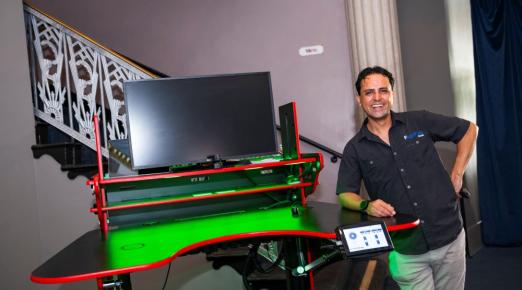 A photo of Vico Hernandez standing next to his innovative ErgoFlex Desk at regional commencement.