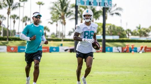 A photo of Robert Prince (left) training and coaching a team member of the NFL's Miami Dolphins on a practice field.