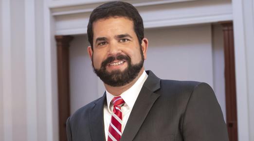 Dr Carvajal wearing a suit with a red and white striped tie smiling