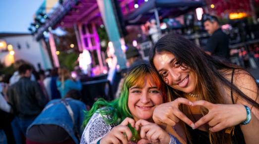 A photo of two students shaping their hands into the shape of hearts in front of the stage at Lumberjack Weekend 2024. 