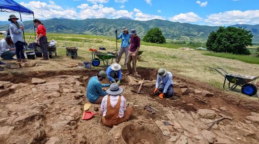 People excavating at a mountain dig site, surrounded by rocky terrain and tools for archaeological work
