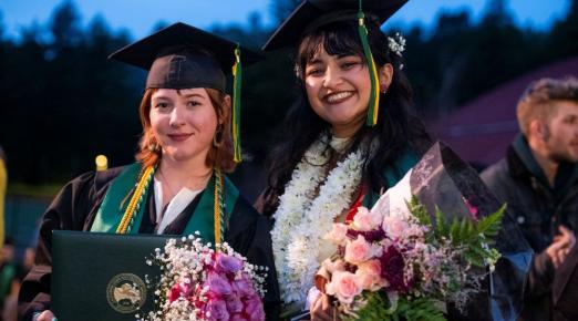 A photo of two graduates posing for a photo outside of the Kinesiology & Athletics building after Fall Commencement.
