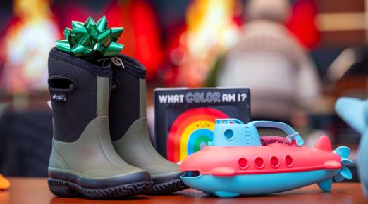 A photo of a pair of rainboots and toys sitting on a table waiting to be wrapped into Winter Wishes gifts. 