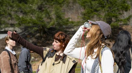 one student points stright ahead and another looks toward the sky through a device