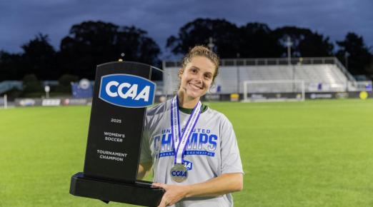 A photo of Cal Poly Humboldt women's soccer player Josie Wolitzky holding the CCAA Women's Tournament trophy. 