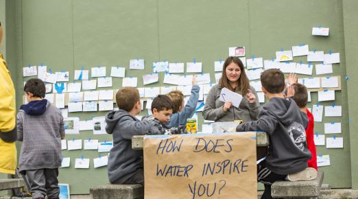children sitting at a bench with a sign attached to it that reads, "how does water inspire you?"
