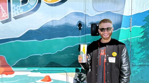 A photo of Carlo Solis standing in front of the mobile alumni center holding the Cal Poly Humboldt koozie during the Forever Humboldt at the San Francisco Giants game. 