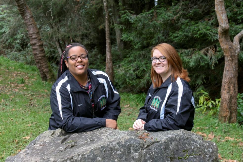 Left to right: Alexis Brown (‘19, Political Science) and Allison Rafferty (‘19, Biology) HSU debate team alumni posing in their debate team jackets leaning on a bolder.