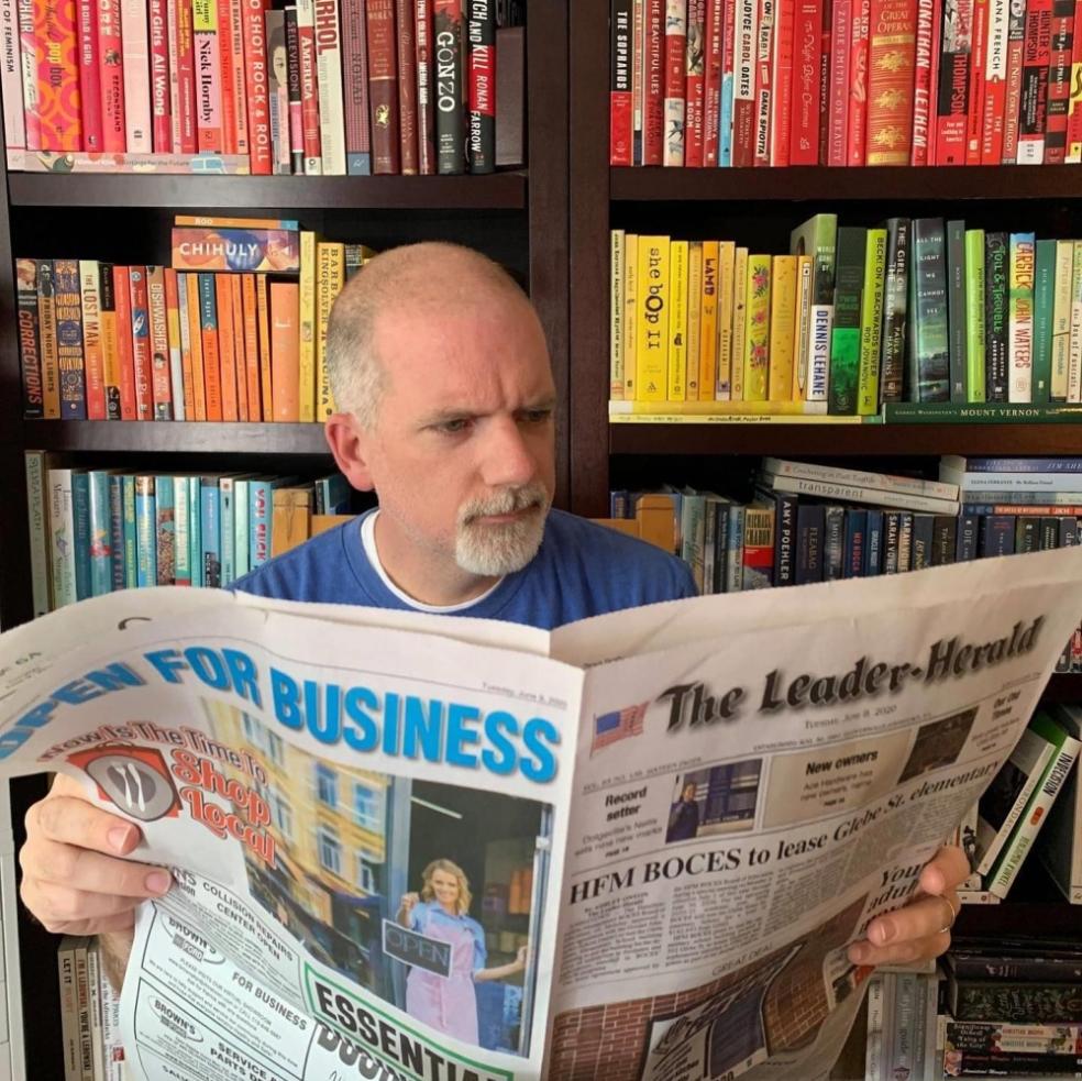 A man reading a paper in front of books.