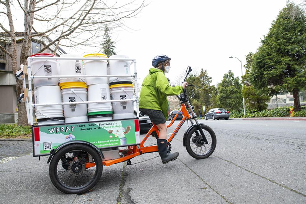 WRRAP student on a bike towing compost bins for food scraps.