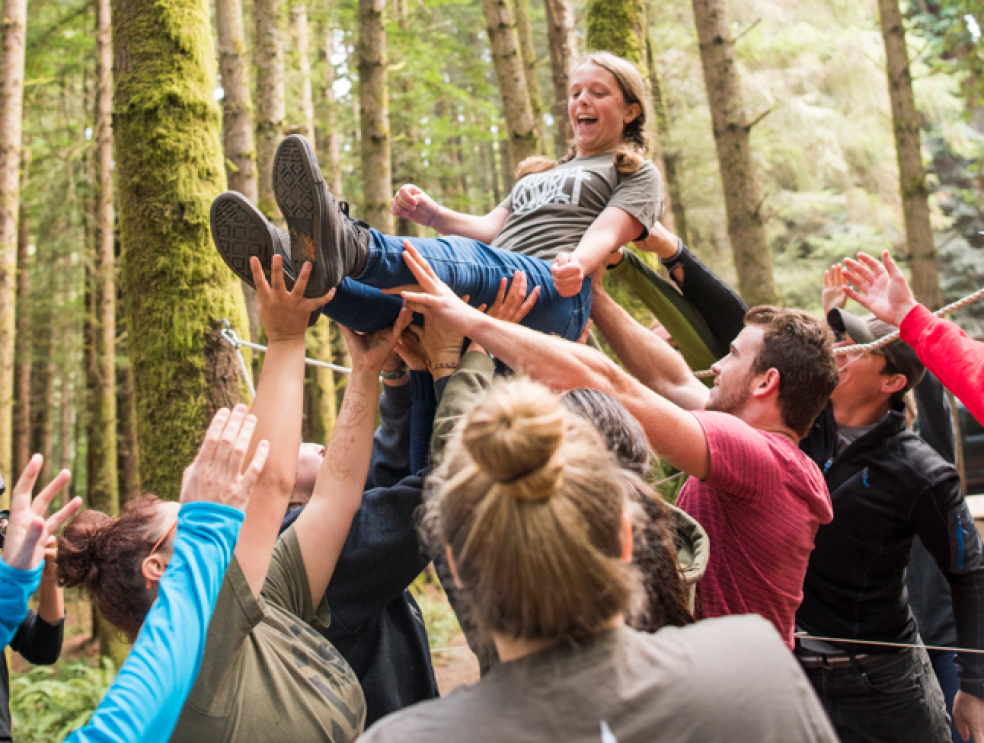 Together, we boldly rise! A photo of Cal Poly Humboldt students holding up another student in the forest.